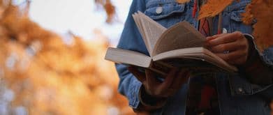 a person holding a book with foliage in the background