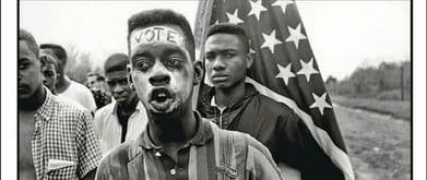 young man with the word 'vote' written on his forehead stands in front of an american flag