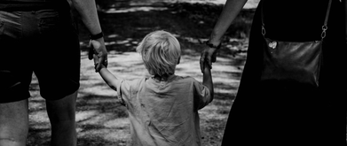 a black and white photo of a little boy walking between his parents while holding their hands