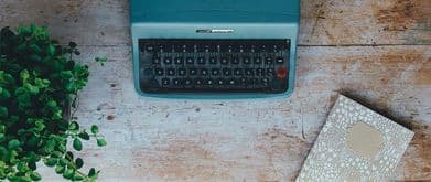 a typewriter lies on a desk beside a notebook