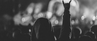 Person in a hood holding up devil hand at a concert. 