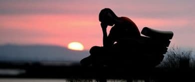 man sitting on bench with his hand on his forehead sadly