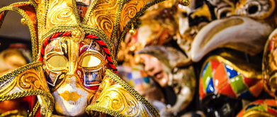 gold and red venetian carnival mask among a pile of other colorful masks