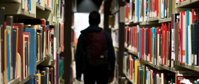 the back of a man walking down a book aisle in a library